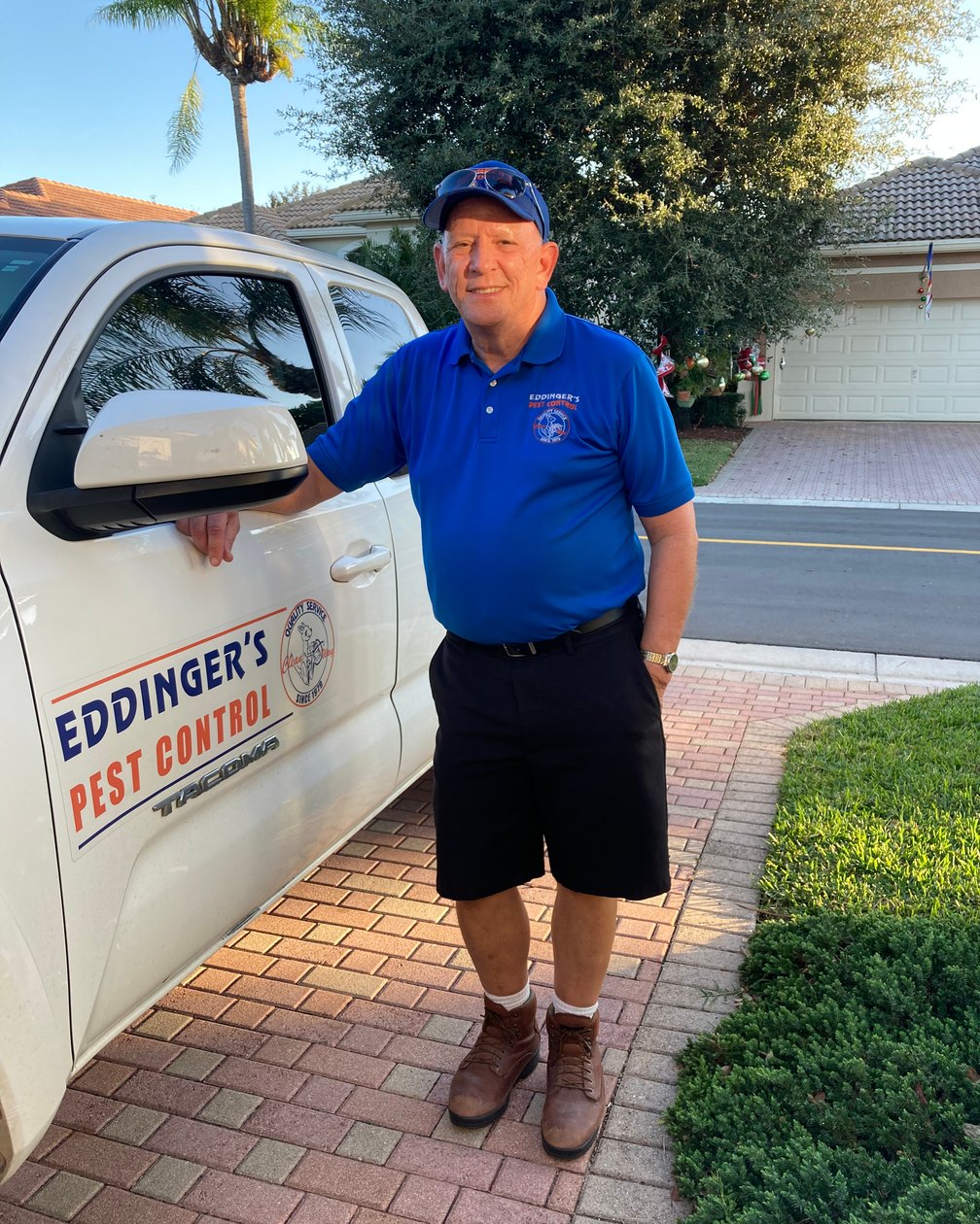 An Eddinger's Pest Control technician in a blue Eddinger's polo and cap standing beside a white service truck with Eddinger's Pest Control lettering